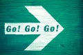 Go! Go! Go! ahead motivational goal text written on white directional arrow pointing towards right painted green wood